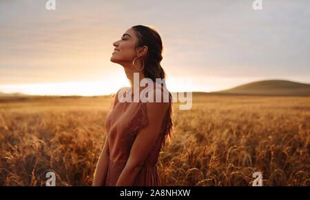 Junge Frau im Weizenfeld suchen entspannt. Frauen in einem landwirtschaftlichen Gebiet während des Sonnenuntergangs. Stockfoto