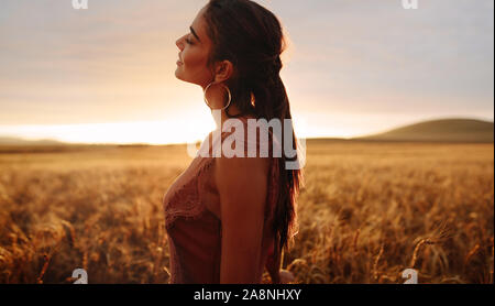 Weibliche am Weizenfeld während des Sonnenuntergangs. Junge Frau in einem landwirtschaftlichen Gebiet geniessen die frische Luft. Stockfoto