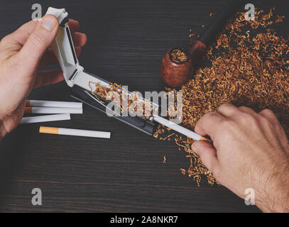 Man macht eine Zigarette mit rollenden Maschine, Hände, Nahaufnahme Stockfoto