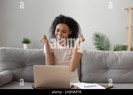 Glückliche afroamerikanische Frau vom Erfolg begeistert, mit Laptop Stockfoto