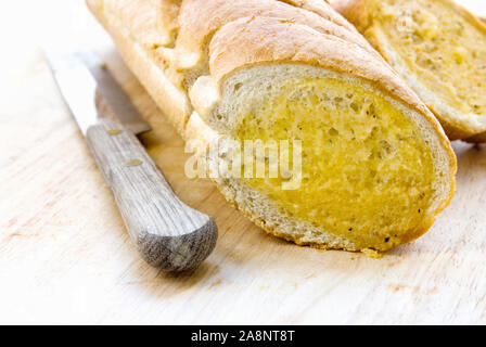 Geschnittenem geröstetem Knoblauch Baguette serviert auf einem hölzernen Schneidebrett und ein altes Messer aus verlegen zur Seite. Stockfoto