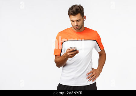 Attraktiven jungen männlichen Athleten im Sport T-Shirt, laufen, für maraphon vorbereiten, tragen Drahtlose Ohrhörer, halten Smartphones, Musik suchen, anhören cardio Stockfoto