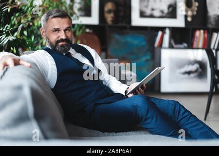 Lächelnd Geschäftsmann mit digitalen tablet Sitzen auf einem Sofa Stockfoto