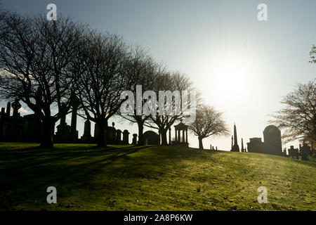 Die sonnigen Herbsttag der Viktorianischen Friedhof Nekropole im Vereinigten Königreich fotografiert von weitem mit der Sonne Hintergrundbeleuchtung. Schwarz Friedhof Silhouette Stockfoto