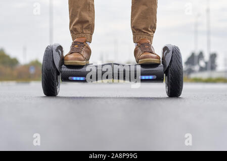 Mann mit Hoverboard auf asphaltierten Straße, ganz nah. Füße auf elektrische Roller outdoor, Vorderansicht Stockfoto