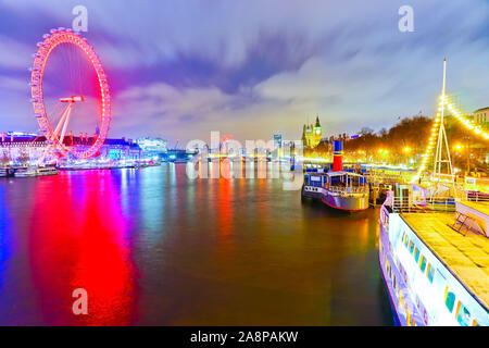 Blick auf die Häuser des Parlaments und London Eye entlang der Themse in London in der Nacht. Stockfoto