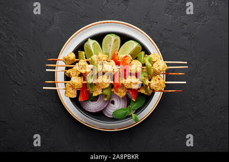 Chicken Tikka auf Spieße in schwarz Schüssel am dunklen Schiefer Hintergrund. Chicken Tikka ist eine indische Küche Teller mit gegrilltem Hühnerfleisch mit Gemüse und Stockfoto
