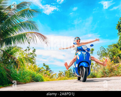 Crazy lustige Frau mit fliegenden Haare Motorrad fahren auf einem blauen Himmel und grüne Tropen Hintergrund. Junge bizarre Mädchen mit dunklen Haaren in Sonnenbrille auf ein Stockfoto