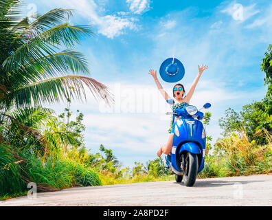 Crazy lustige Frau mit fliegenden Haare Motorrad fahren auf einem blauen Himmel und grüne Tropen Hintergrund. Junges Mädchen mit dunklen Haaren in Sonnenbrille auf einem blauen Stockfoto