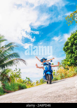 Crazy lustige Frau mit fliegenden Haare Motorrad fahren auf einem blauen Himmel und grüne Tropen Hintergrund. Junge bizarre Mädchen mit dunklen Haaren in Sonnenbrille auf ein Stockfoto