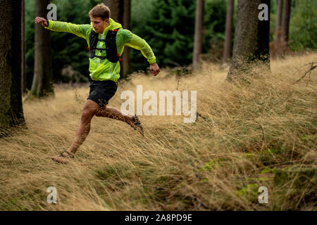 Ein junger Athlet in Barfuß Schuhe läuft den Berg hinunter. Die Berge laufen. Querfeldein laufen. Einzelnen Sport Stockfoto