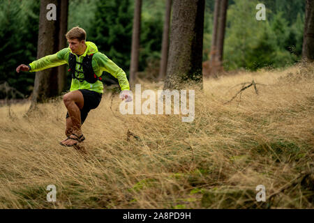 Ein junger Athlet in Barfuß Schuhe läuft den Berg hinunter. Die Berge laufen. Querfeldein laufen. Einzelnen Sport Stockfoto