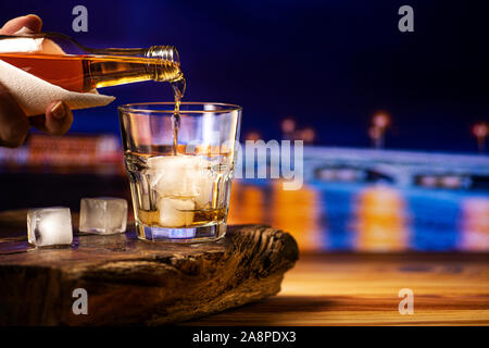 Gießt Whiskey in ein Glas mit Eis. Ein Glas alkoholisches Getränk auf einer hölzernen Tisch. Stockfoto