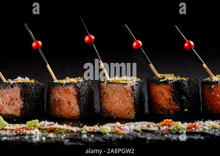 Gebeizter Lachs in Scheiben geschnitten in Schwarz, mit Paniermehl Spieße auf eine schwarze Platte gelegt. Fusion Food Konzept, Low Key, copy Space Stockfoto