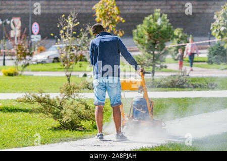 Arbeitnehmer, die mit einer speziellen Maschine schmalen Straße in der City Park. Stockfoto