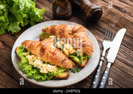 Frühstück Croissant Sandwich mit Rührei, Käse und Salat auf hölzernen Tisch Stockfoto
