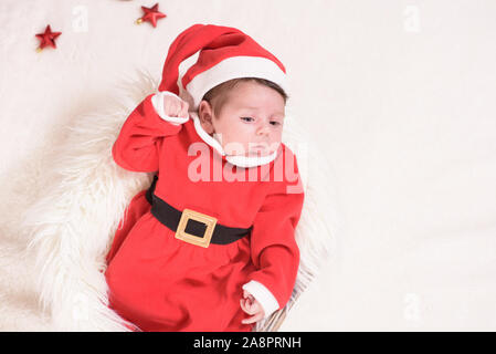 Kleines Mädchen gekleidet, wie Santa Claus in einem Korb liegen mit einer weißen Decke. freier Speicherplatz. Weihnachten Konzept. Stockfoto