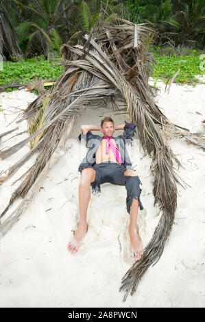 Castaway Geschäftsmann, der in einem provisorischen Strandhüttenheim zurückliegt Stockfoto