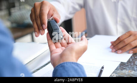 Geschäftskonzept, Kfz-Versicherung, Auto verkaufen und kaufen, Kfz-Finanzierung, Kfz-Schlüssel für Kfz-Kaufvertrag. Neue Besitzer nehmen Schlüssel von männlichen Salespe Stockfoto