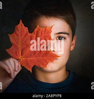 Close up Portrait von Jungen die Hälfte seines Gesichtes mit einem Maple Leaf. Stockfoto