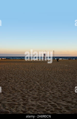 Ein roter Himmel bei Sonnenuntergang über dem Pazifischen Ozean und eine einsame Palme am Newport Beach in Kalifornien. Die Rettungsschwimmer sind für den Tag beendet Stockfoto