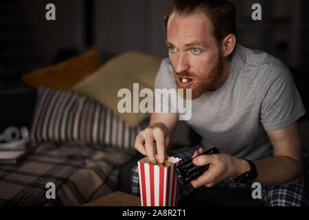 Portrait von bärtigen erwachsenen Mann Fernsehen in dunklen und essen Pop Corn und genießen Sie bis spät in die Nacht Filme, Kopie Raum Stockfoto