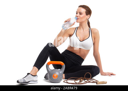 Frau trinkt Wasser aus der Flasche nach dem Workout, isoliert auf weißem, Hydratation Stockfoto