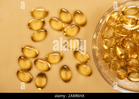 Blick von oben auf die glänzenden goldenen Fisch Öl Kapseln aus Glas Schüssel auf gelben Hintergrund verstreut Stockfoto