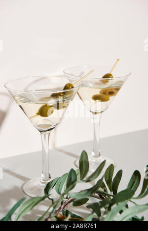 Gläser mit Martini und Olive Branch auf graue Oberfläche auf weißem Hintergrund Stockfoto