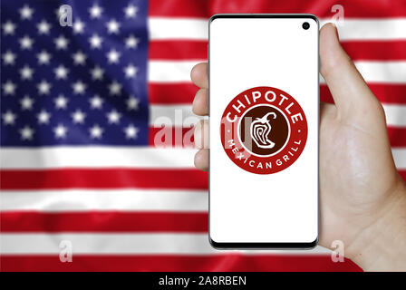 Logo der öffentlichen Unternehmen Chipotle Mexican Grill angezeigt auf einem Smartphone. Flagge der USA Hintergrund. Credit: PIXDUCE Stockfoto