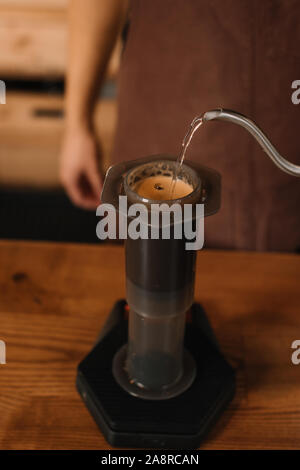 7/8-Ansicht von Barista gießt Wasser aus dem Wasserkocher in aeropress während Kaffee vorbereiten Stockfoto