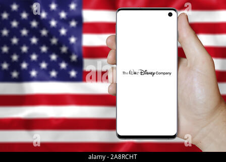 Logo der öffentlichen Unternehmen der Walt Disney Company auf dem Smartphone angezeigt. Flagge der USA Hintergrund. Credit: PIXDUCE Stockfoto