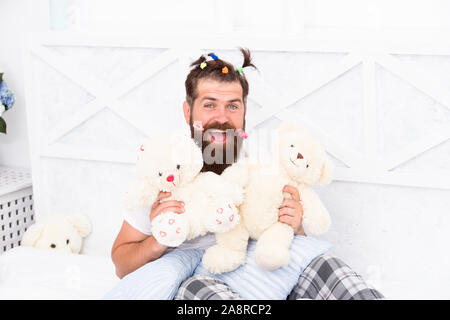 Bärtiger Mann spielen mit Bär Spielzeug. happy Dad entspannende Schlafzimmer. Vater mit lustigen Frisur. freaky Hipster im Bett entspannen. bleiben Sie den ganzen Tag im Bett. Zeit zu Hause zu entspannen. glückliche Vaterschaft. Inspiriert zu spielen. Stockfoto