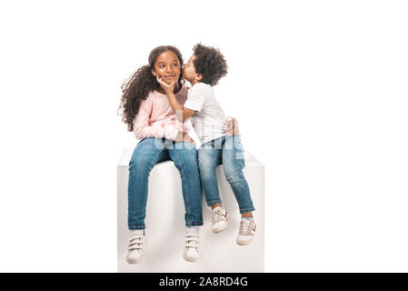 Cute African American Boy küssen adorable Schwester sitzend auf White Cube zusammen isoliert auf weißem Stockfoto