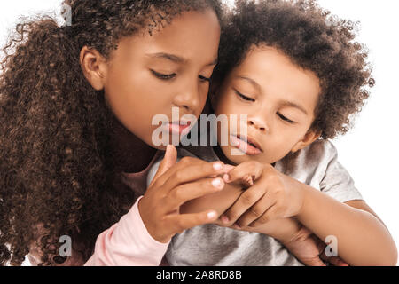Aufmerksame afrikanische amerikanische Schwester an der Hand von adorable Bruder auf Weiß isoliert Stockfoto