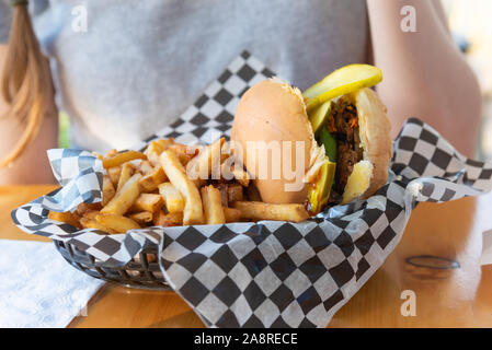 In der Nähe von Korb Holding vegan schwarz-bean Burger und Pommes frites auf der Outdoor Terrasse Tisch Stockfoto