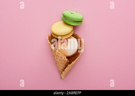 Blick von oben auf die bunten köstlichen französischen Makronen in knuspriger Waffel Kegel auf rosa Hintergrund Stockfoto