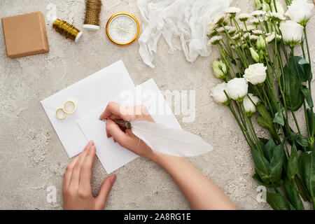 Blick auf Frau schreiben auf leeren in der Nähe der Hochzeit Ringe, Kompass, Gaze, Blumen und Geschenk Box auf strukturierte Oberfläche 7/8 Stockfoto