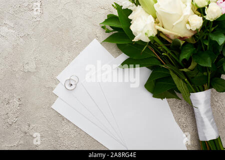 Ansicht von oben in Silber Ringe auf Einladung Karten in der Nähe von Bouquet auf strukturierte Oberfläche Stockfoto