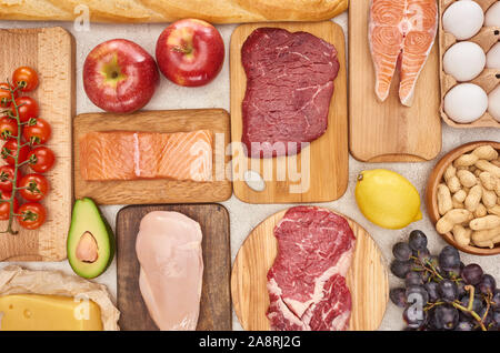 Blick von oben auf die sortierten Fleisch, Geflügel, Fisch, Eier, Obst, Gemüse, Käse und Baguette auf hölzerne Schneidbretter Stockfoto