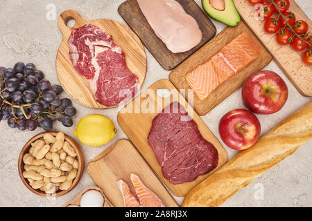 Ansicht von oben af organischen verschiedene Fleisch, Geflügel, Fisch, Äpfel, Trauben, Zitronen, Avocado, Tomaten und Erdnüssen auf Holz Schränke mit frischem Baguette auf m Stockfoto