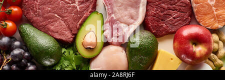 Panorama-aufnahme von rohem Fleisch, Fisch und Geflügel in der Nähe von Avocados, Tomaten, Traube, Apfel Käse und Erdnüsse Stockfoto