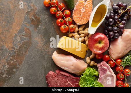 Blick von oben auf die rohen Fisch, Fleisch und Geflügel, die in der Nähe von Gemüse, Obst, Käse, Erdnüsse, Kräuter und Olivenöl auf Marmor Oberfläche mit Kopie Raum Stockfoto