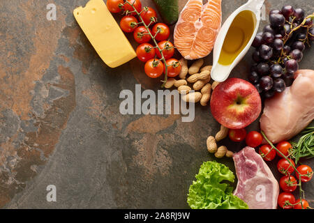 Blick von oben auf die rohen Fisch, Fleisch und Geflügel, die in der Nähe von Gemüse, Obst, Käse, Erdnüssen und Olivenöl auf Marmor Oberfläche mit Kopie Raum Stockfoto