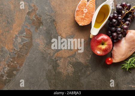 Blick von oben auf die rohen Fisch und Geflügel in der Nähe von Gemüse, Obst, Kräuter Zweige und Olivenöl auf Marmor Oberfläche mit Kopie Raum Stockfoto