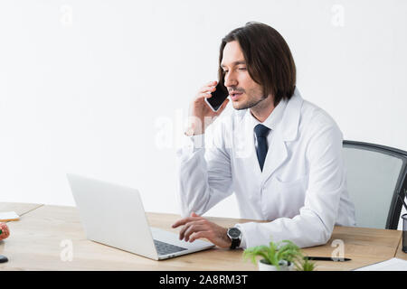 Ruhe Arzt sprechen auf dem Smartphone während der Sitzung in hellen Büro mit Laptop auf dem Tisch Stockfoto