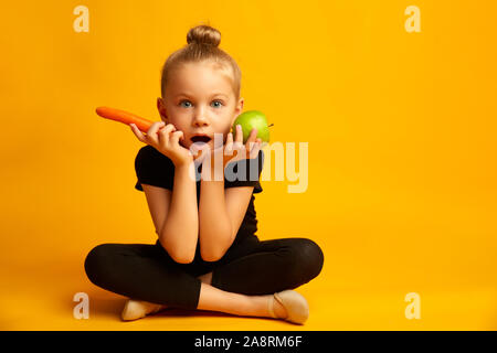 Kleine Tänzerin die Wahl zwischen einem grünen Apfel und Karotte verwirrt Stockfoto