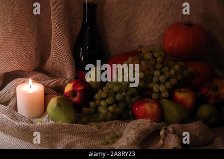 Herbst ernte noch leben. Äpfel, Birnen, Trauben und Kürbis Sacktuch Hintergrund mit einer Flasche Wein und Kerzenschein Stockfoto