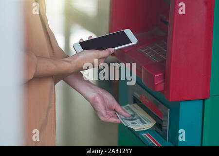 Frau mit der Smart Mobile Phone für das Zurückziehen vor der ATM Automatic Teller Machine, Business Konzept Stockfoto