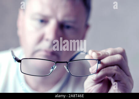 Porträt einer müde Mann mit Brille in den Händen. Mann sieht durch die Brille. Weißer Mann und Brillen in Händen. Selektiver Fokus Stockfoto